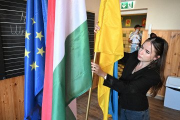 A woman adjusts the EU, Hungarian and Ukrainian flag at the newly established Taras Shevchenko bilingual primary school for ethnic Ukrainians on the first school day in Budapest on September 1, 2025. (Source: Getty Images)