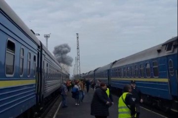 Passengers stand between trains as smoke rises near a railway station following a Russian attack. (Source: Pivden)