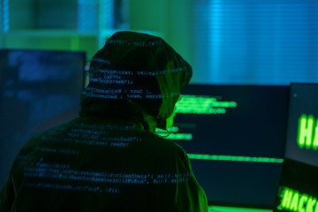 A view of a hooded hacker organizing a massive data breach attack on corporate servers in a dark location. Illustrative photo. (Source: Getty Images)
