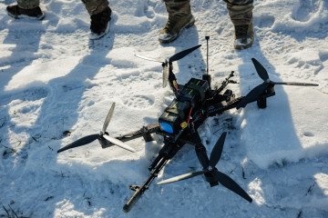 An FPV drone with a Kalashnikov rifle attached to it lies in the snow. (Source: Getty Images)