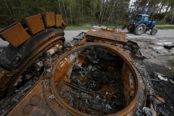 Tractor pasando junto a vehículos militares rusos destruidos en un campo de la región de Kyiv durante la guerra en Ucrania.
