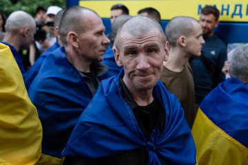 A Ukrainian soldier, with a shaved head and draped in a Ukrainian flag, smiles following his release during a prisoner exchange on May 23, 2025. (Source: Getty Images)