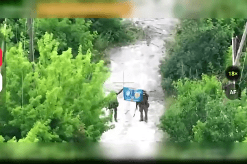 A drone camera view shows two Ukrainian soldiers holding up a flag on a path surrounded by dense greenery in the village of Novokhatske. (Source: 37th Separate Marine Brigade)