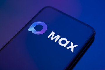 The Max logo appears on a smartphone screen placed on a reflective surface onto which a gradient of blue and purple is projected. Illustrative photo. (Source: Getty Images)