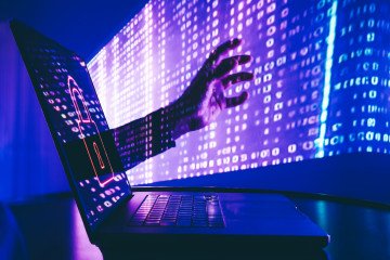 A visual representation of a cyberattack, with binary code projected on a hand reaching towards a laptop. Illustrative photo. (Source: Getty Images)