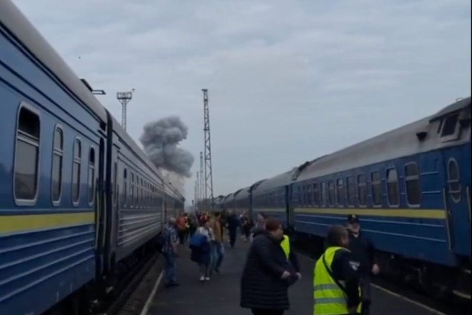 Passengers stand between trains as smoke rises near a railway station following a Russian attack. (Source: Pivden)