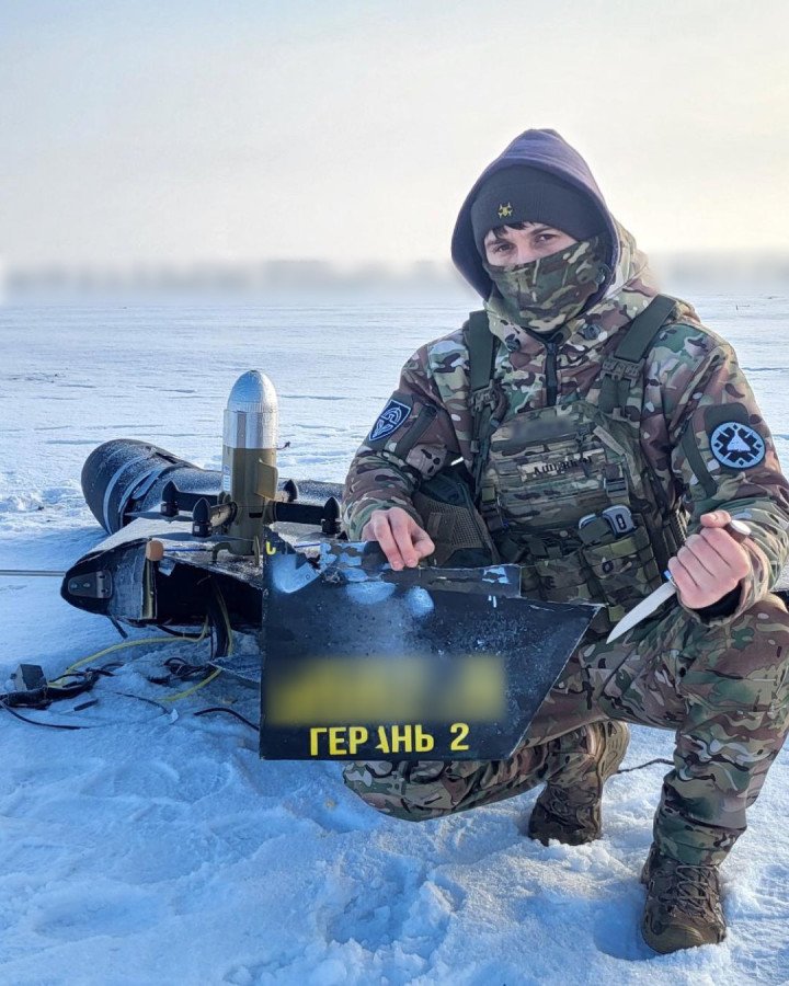 A Ukrainian soldier poses with debris from a downed Russian Geran-2 (Shahed) drone, intercepted by a Sting drone in a snowy field. (Photo: Wild Hornets)