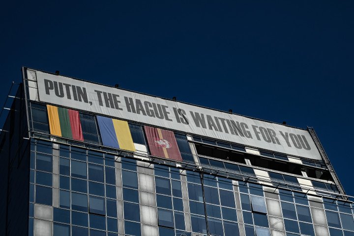 A large banner is displayed on top of a building reading ''[Vladimir] Putin, [the International Court of Justice of] The Hague is waiting for you'' alongside the Lithuanian, Ukrainian, and Vilnius flags in Vilnius, Lithuania, on April 22, 2026.