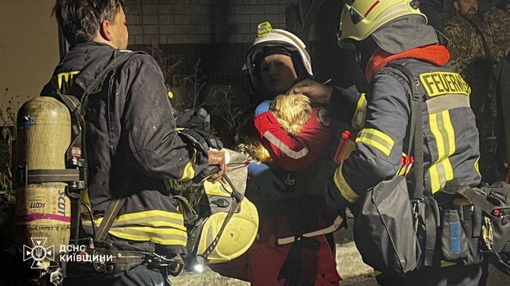 Los servicios de emergencia ucranianos ayudan a un niño que sostiene a un perro pequeño después de evacuarlos de un edificio residencial alcanzado durante un ataque con drones rusos en Vyshhorod. (Fuente: DSNS Región de Kyiv)