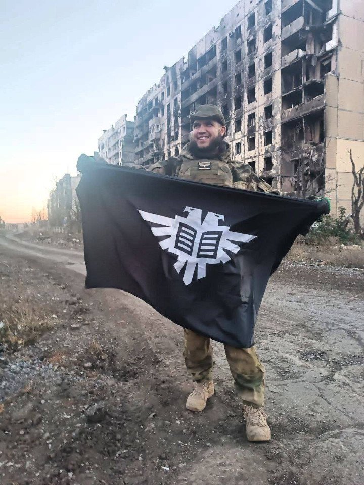 Russian soldier poses with Black 100 flag on the frontlines inside Ukrainian territory. (Source: Black 100)