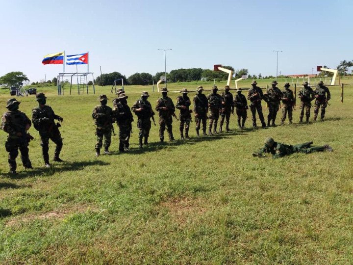 A line of Cuban and Venezuelan military personnel stand in formation on a field with the Venezuelan and Cuban flags visible in the background, following the announcement of joint operations between Avispas Negras and Venezuela’s Fuerza de Acciones Especiales. (Photo: Open source)