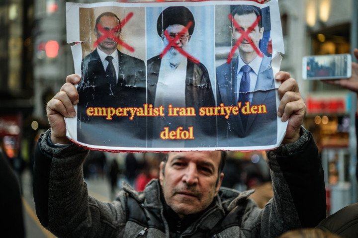 A Syrian man holds a poster of (L-R) Russian President Vladimir Putin, Iranian Supreme Leader Ayatollah Ali Khamenei and Syrian President Bashar al-Assad reading “Imperialist Iran get out of Syria”. (Photo by OZAN KOSE / AFP) (Photo by OZAN KOSE/AFP via Getty Images) A Syrian man holds a poster of (L-R) Russian President Vladimir Putin, Iranian Supreme Leader Ayatollah Ali Khamenei and Syrian President Bashar al-Assad reading “Imperialist Iran get out of Syria”. (Photo by OZAN KOSE / AFP) (Photo by OZAN KOSE/AFP via Getty Images)