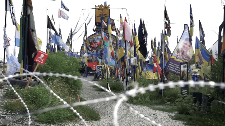 A barbed-wire path leads toward the Donetsk region sign, transformed into a dense memorial of flags, portraits, and unit banners honoring Ukrainians killed in the war. (Source: Support Forces of the Armed Forces of Ukraine) A barbed-wire path leads toward the Donetsk region sign, transformed into a dense memorial of flags, portraits, and unit banners honoring Ukrainians killed in the war. (Source: Support Forces of the Armed Forces of Ukraine)