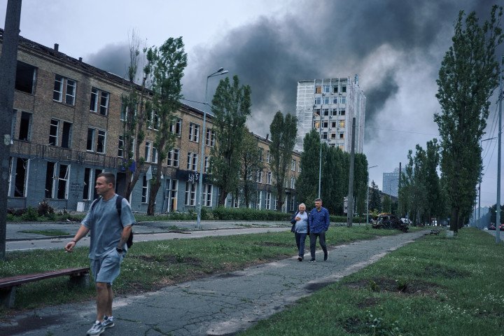 Residents walk past destroyed buildings as smoke billows in the distance following a massive overnight Russian missile and drone attack that struck more than 27 sites across the Ukrainian capital. Kyiv, Ukraine. July 31, 2025. Photo by Josh Olley/UNITED24 Media