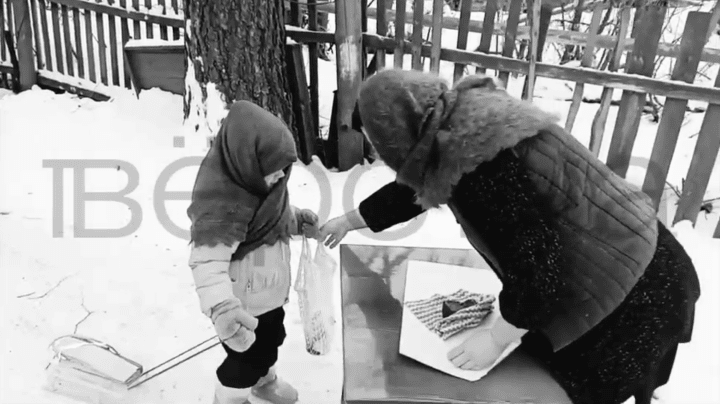 Screenshot from a video filmed in a black-and-white where a child is wearing a woolen scarf and pulling a sled through the snow with string bags to exchange ration cards for bread. (Source: Verstka) Screenshot from a video filmed in a black-and-white where a child is wearing a woolen scarf and pulling a sled through the snow with string bags to exchange ration cards for bread. (Source: Verstka)