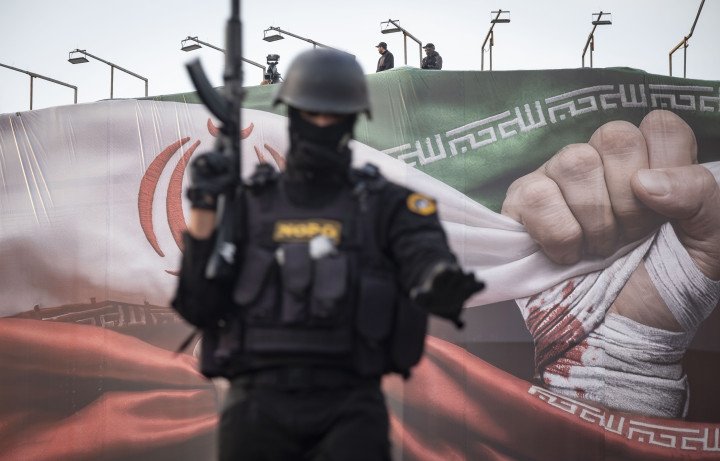 Armed members of Iran's police special forces monitor an area while standing on an armored military vehicle under a country flag during a pro-Government rally in downtown Tehran, Iran, on January 12, 2026. (Photo by Morteza Nikoubazl/NurPhoto via Getty Images)