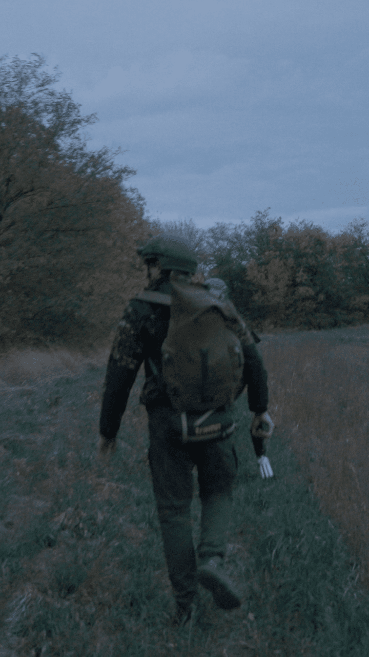 El reportero de UNITED24 Media, Philip Malzahn, camina entre la arboleda al anochecer, portando una pistola de red portátil diseñada para interceptar drones FPV. Foto: Yegor Terletskyi / UNITED24 Media