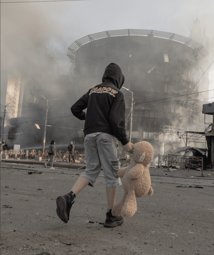 A boy carries a teddy bear past a burning shopping center in Kyiv following Russia’s mass overnight attack on May 24. (Photo: Nikita Lisovyi)