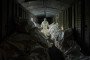 A Ukrainian forensic expert in a white hazmat suit and gas mask stands inside a dark, crowded railway car filled with white body bags of returned dead.