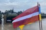 A Latvian and Ukrainian flag wave in front of the vehicles during the handover of 21 Patria 6x6 armored transport vehicles to the Ukrainian armed forces at the Latvian military base in Adazi on November 6, 2025. (Source: Getty Images)