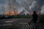 A teenager sits on a bicycle watching flames rise from a burning logistics warehouse following a Russian ballistic missile attack on Kyiv and the surrounding region on August 5, 2026, in Kyiv, Ukraine.